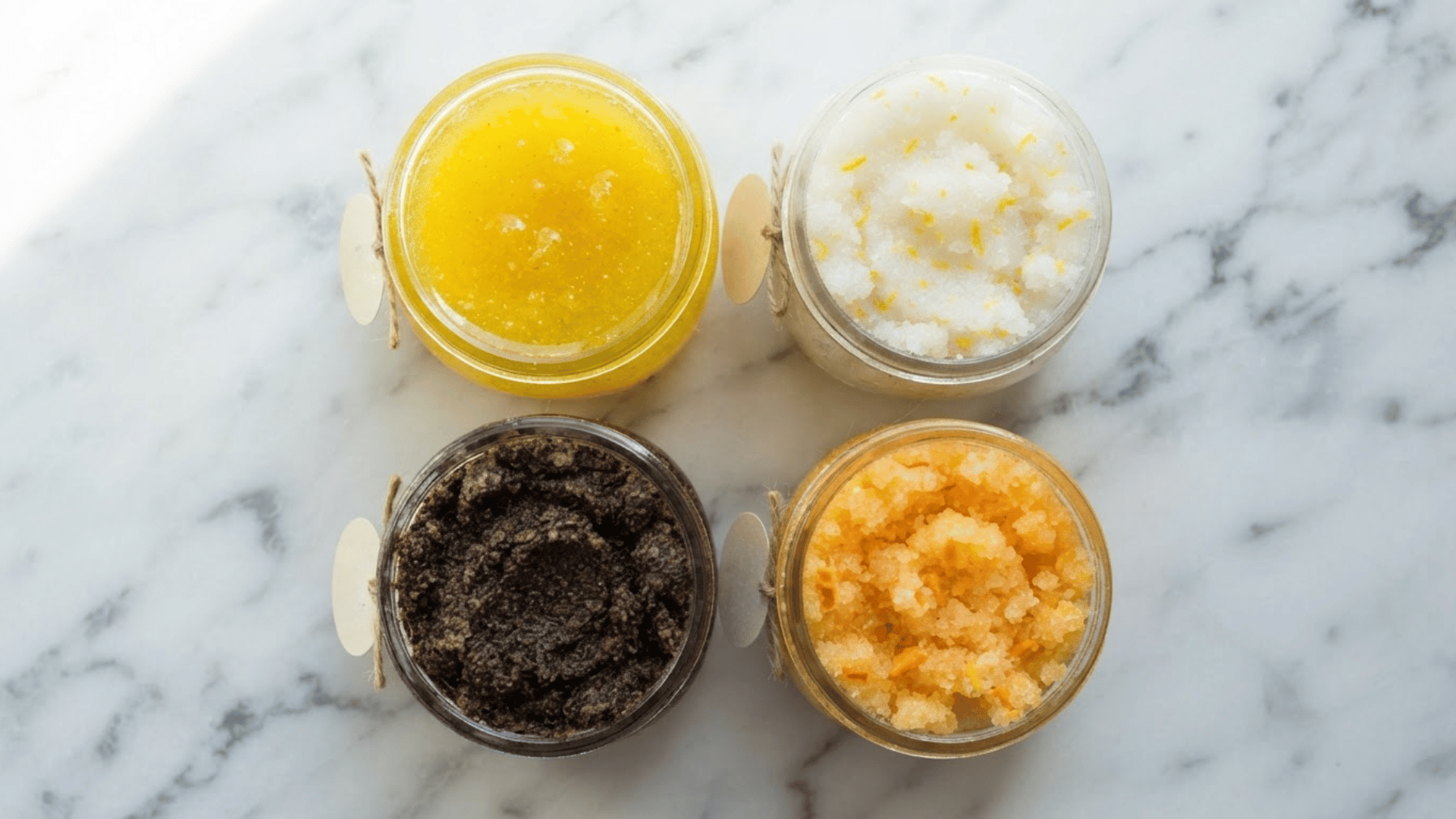 four different homemade body scrubs in glass jars showing different textures