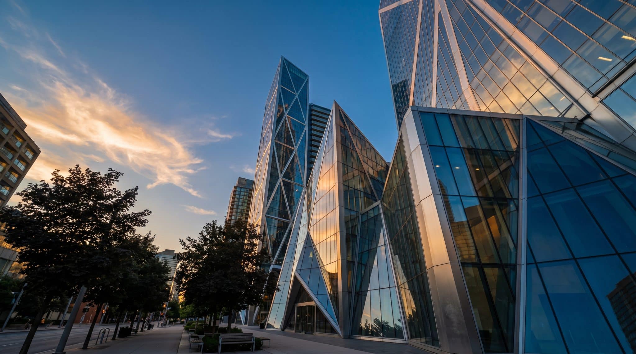Modern skyscrapers with glass facades reflecting sunset, surrounded by trees and urban walkway