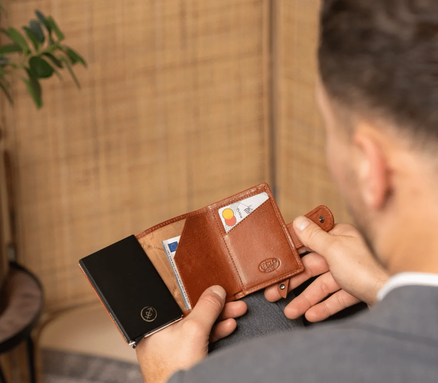Man holding open brown leather wallet displaying credit cards and cash in a cozy room setting