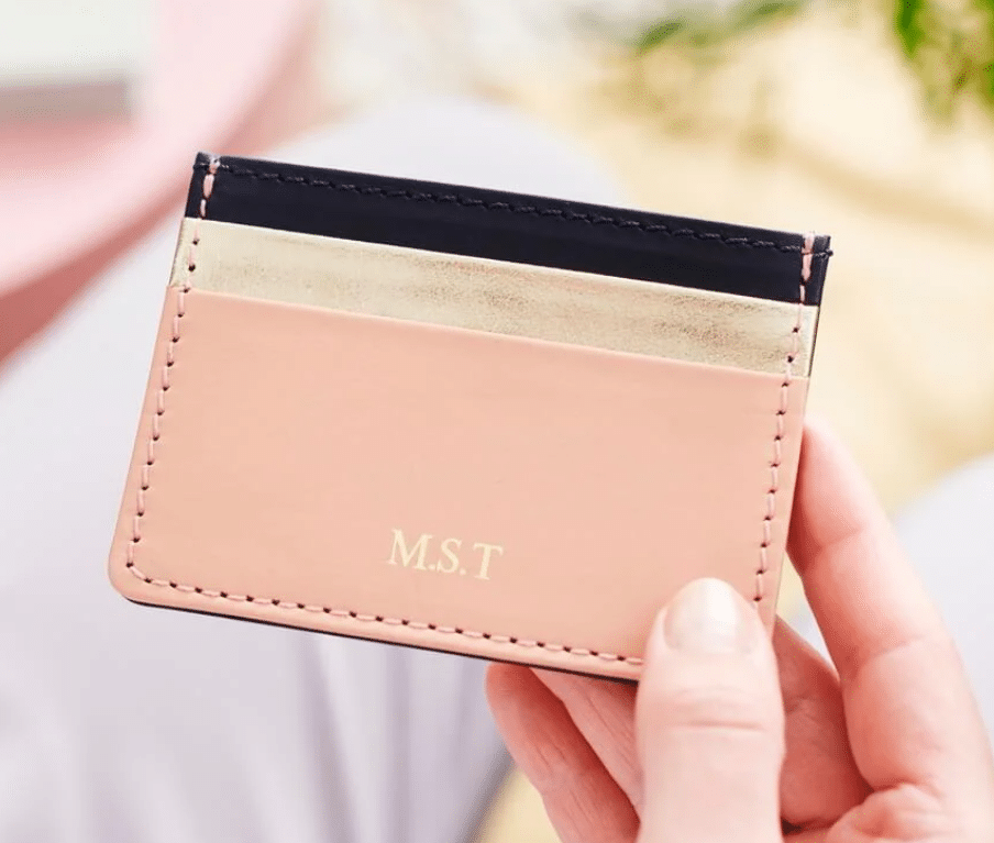 Pink leather card holder with initials, held in hand, soft focus background