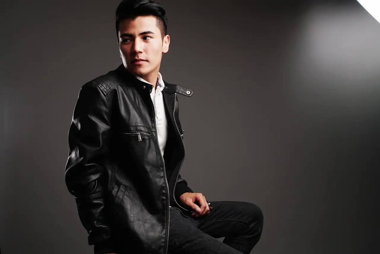 Man in black leather jacket seated in studio with dark background
