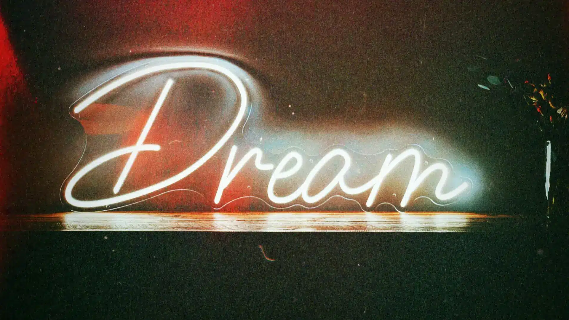 Neon "Dream" sign glowing on dark background with red and white lighting accents