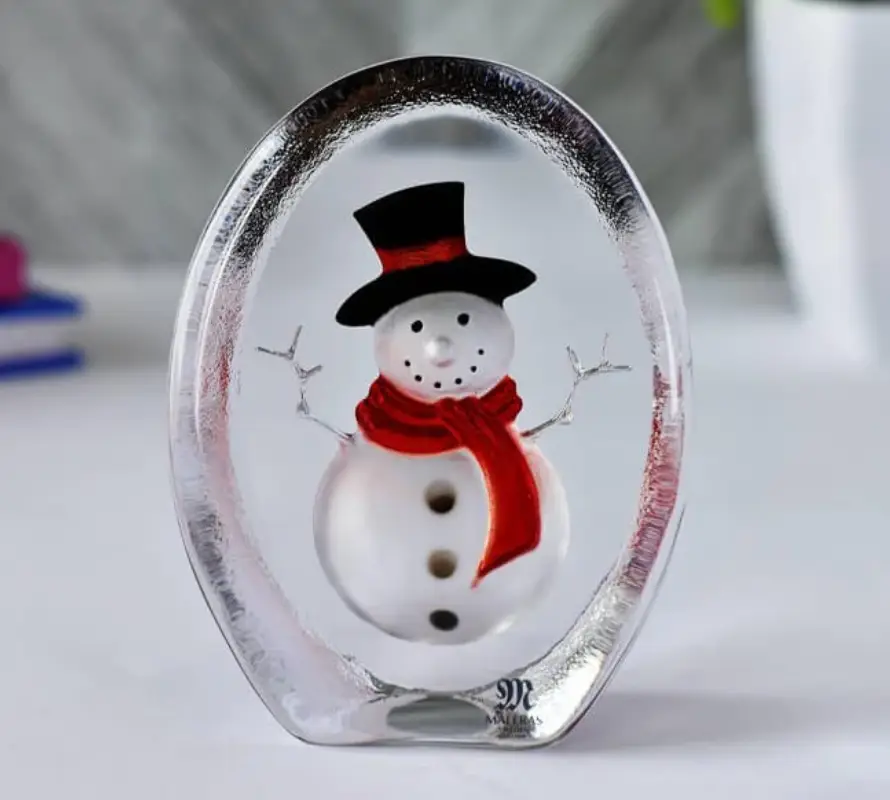 Glass snowman figurine with red scarf and black hat on white surface