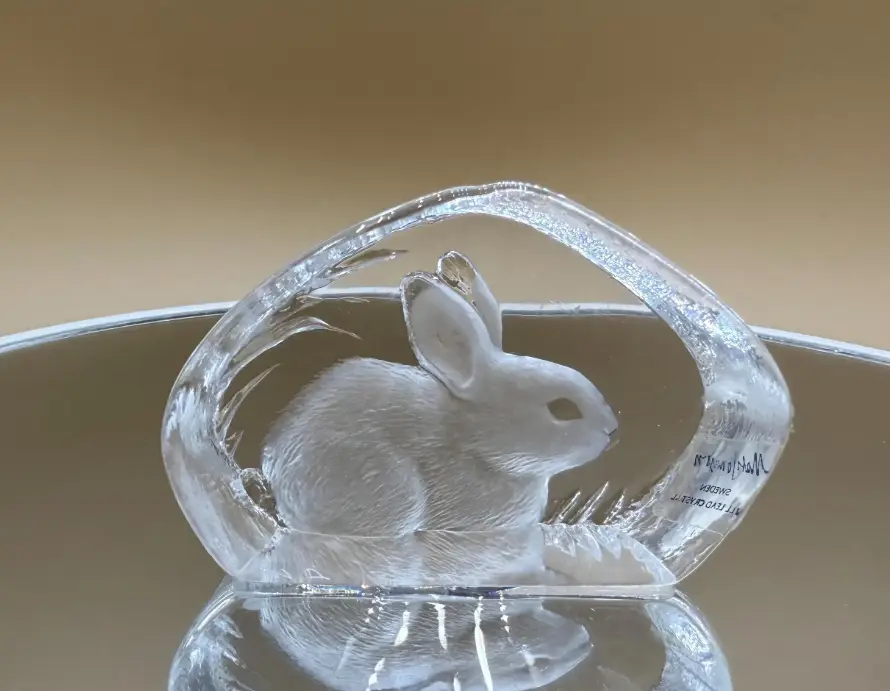 Glass rabbit sculpture on reflective surface with neutral background in soft lighting