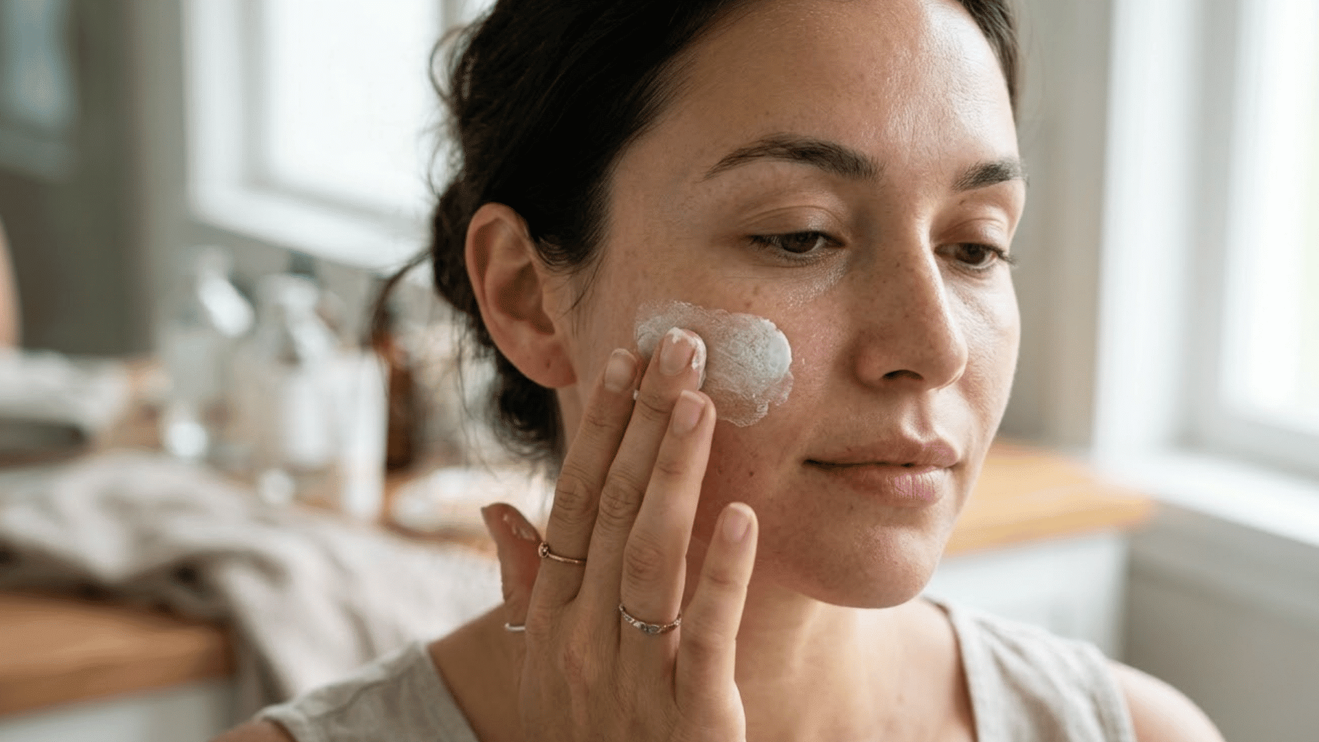 woman applying thick white mineral sunscreen to her cheek in soft natural daylight with realistic skin texture