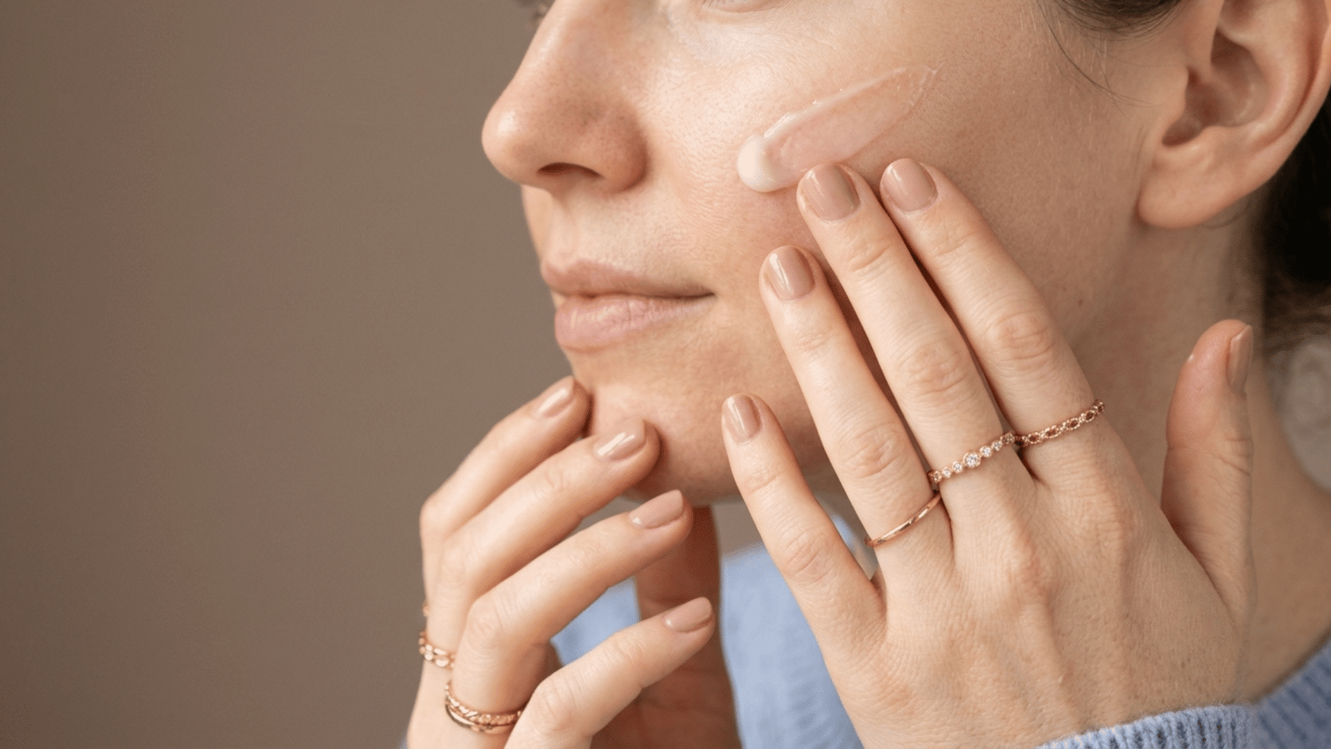 woman applying moisturizer to her cheek with fingertips while preparing skin for foundation
