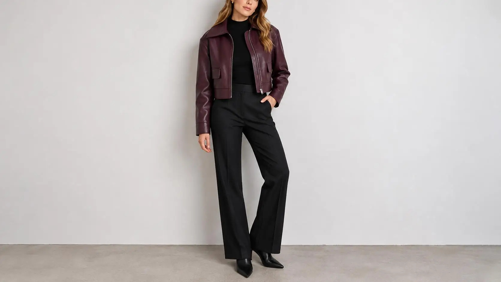 Woman wearing burgundy leather jacket and black pants against plain background