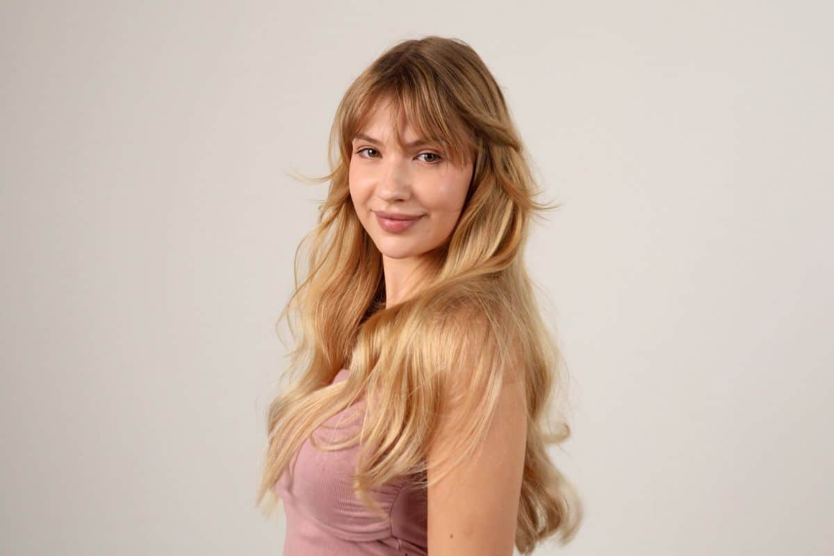 Young woman with long blonde hair in a pastel purple top against a plain background