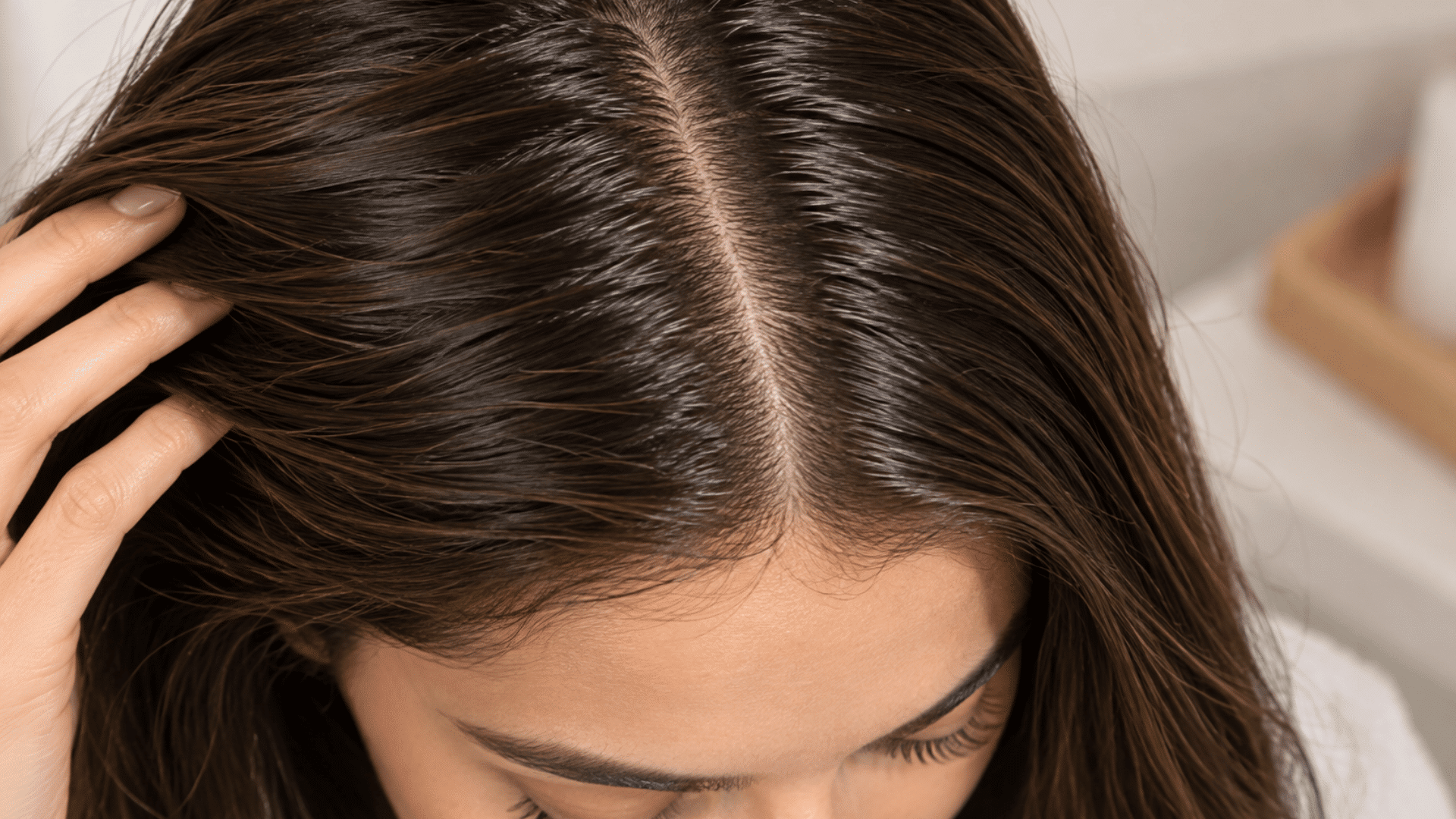 a woman parting her dark brown hair with her hand revealing a clean scalp and visible center hair part