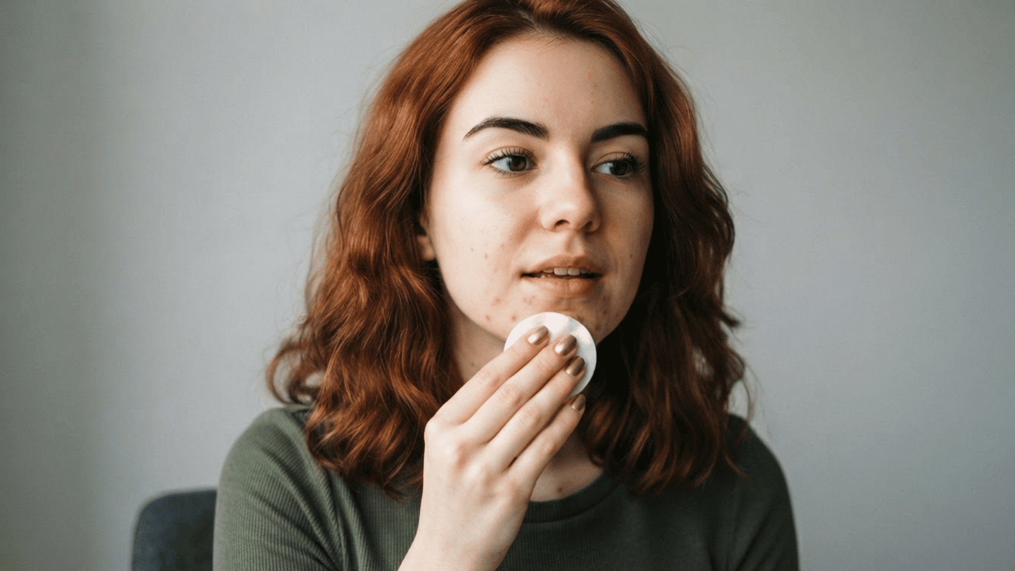 woman blotting excess oil from her chin with a cotton pad during a skincare routine