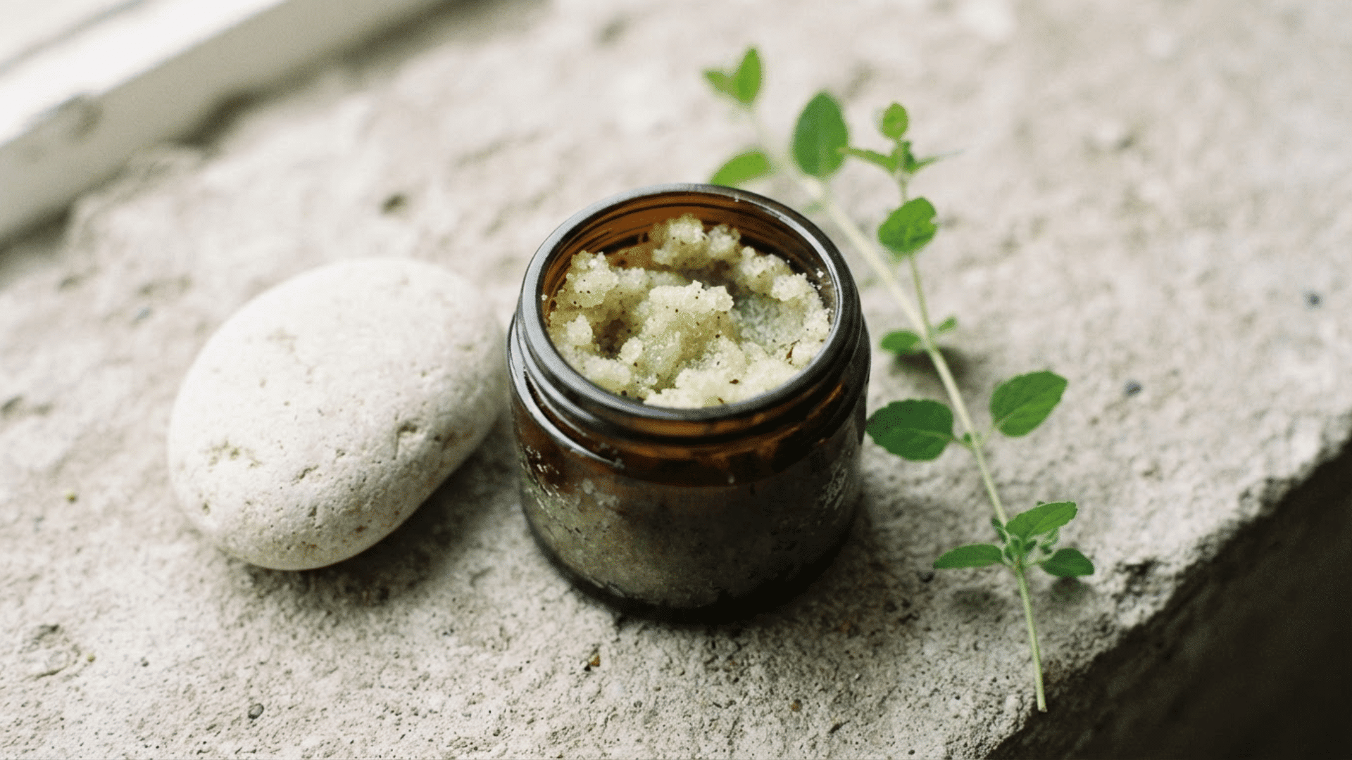 homemade sea salt body scrub in a small amber glass jar with fresh green leaves