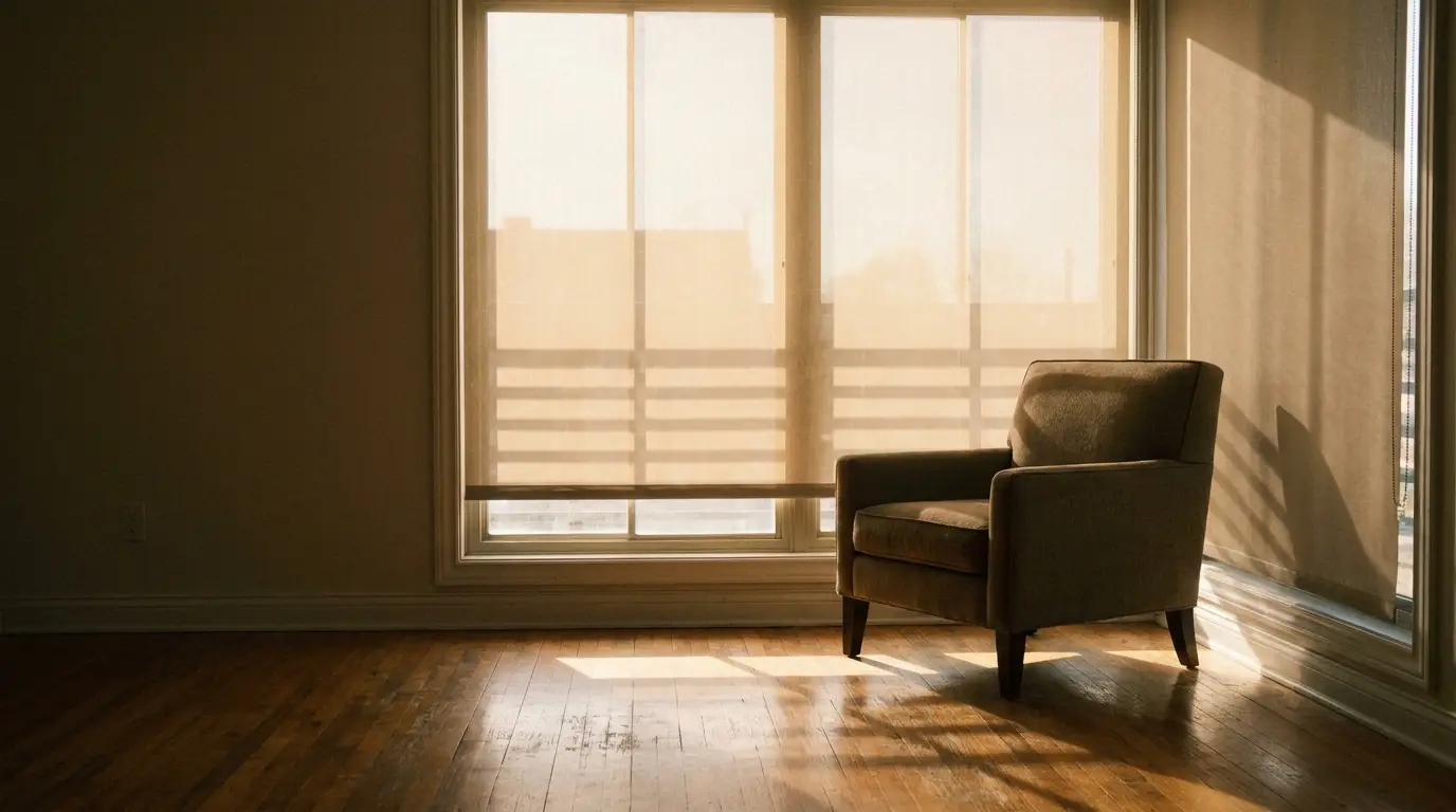 Armchair in sunlit room with wooden floors and large window blinds