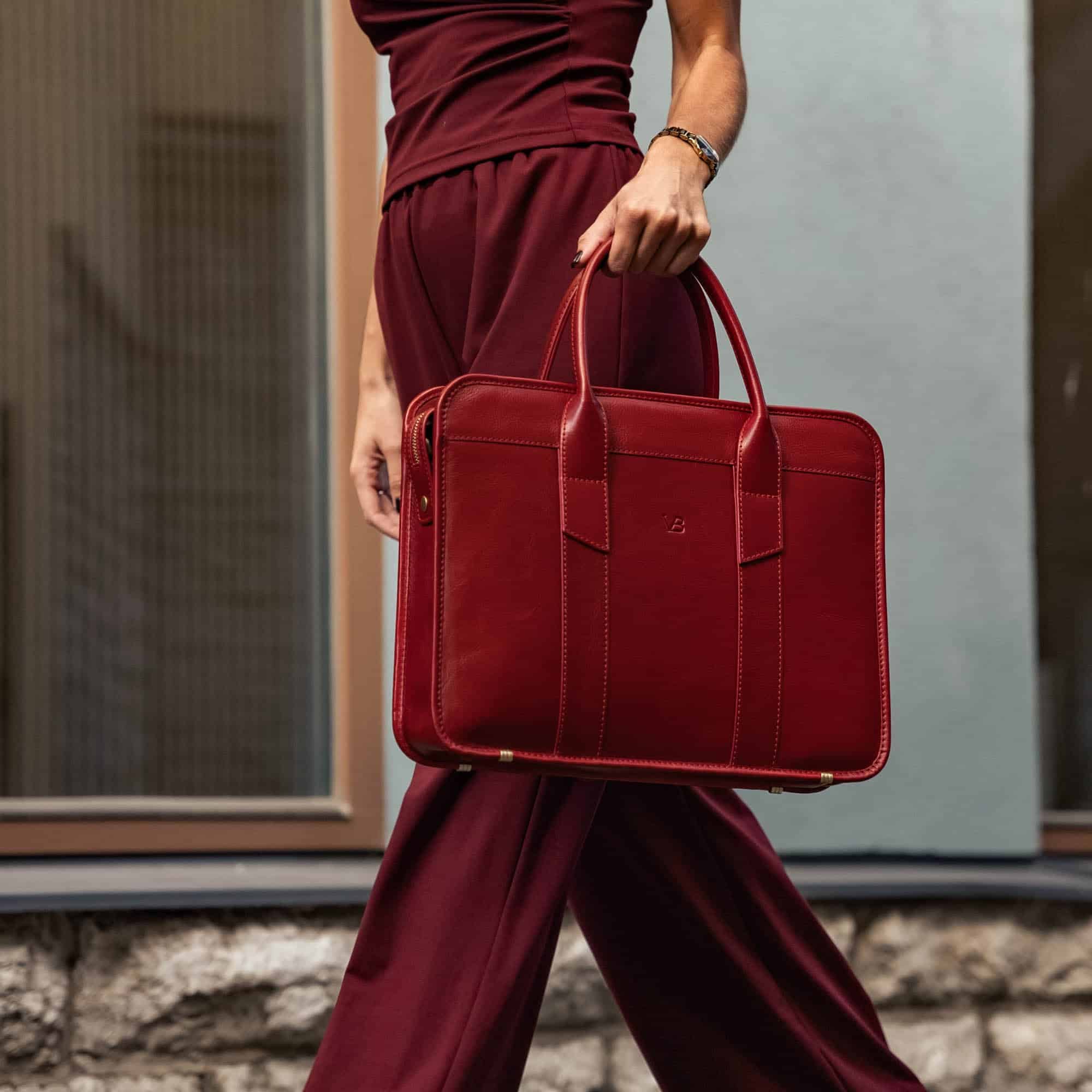 Person holding a red leather briefcase, wearing a matching burgundy outfit, outside a building