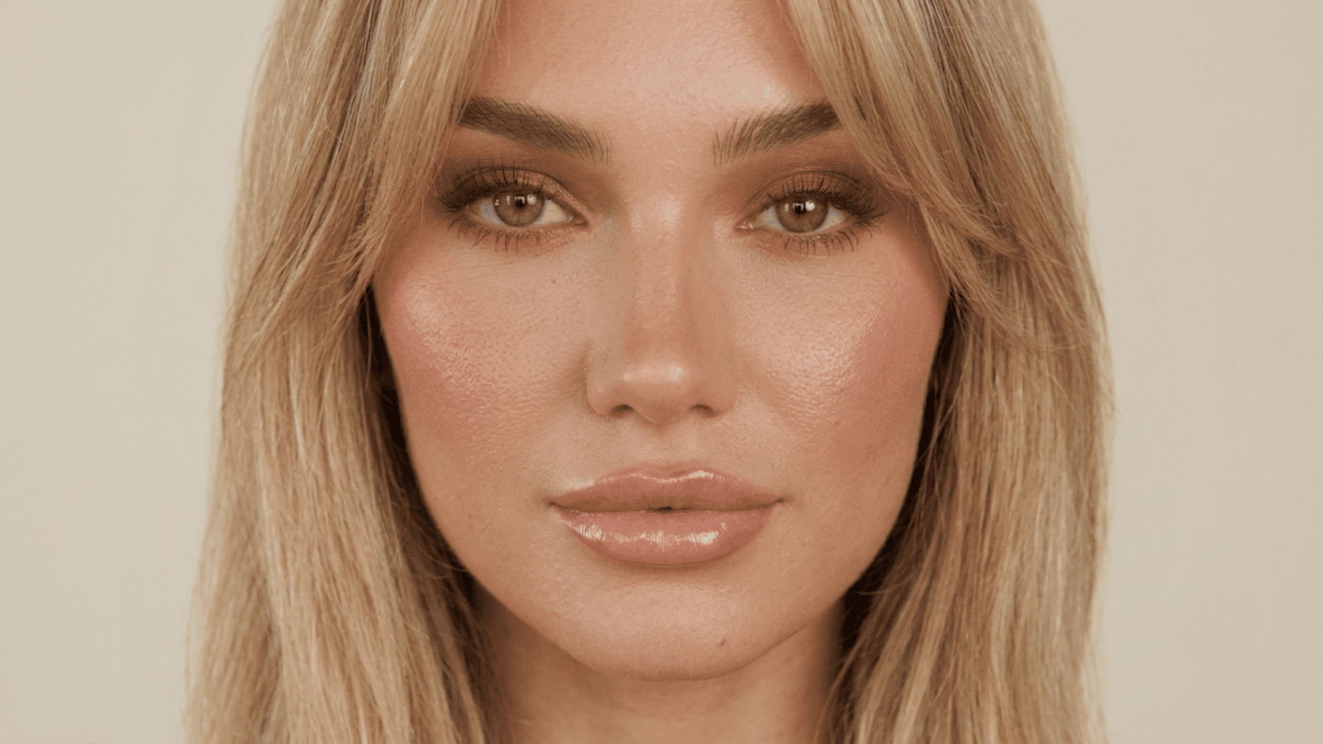 woman with warm bronzed makeup featuring caramel eyeshadow defined lashes glowing cheeks and glossy nude lips