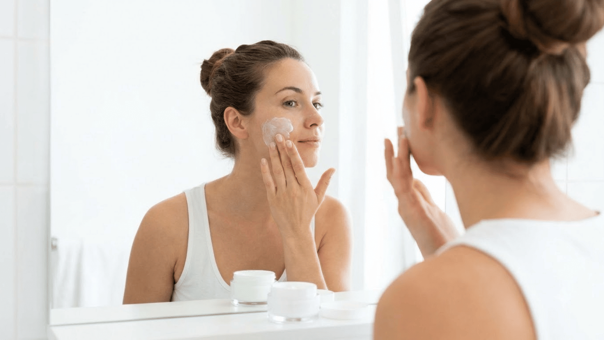 woman applying ceramide face cream while looking in a mirror during her skincare routine