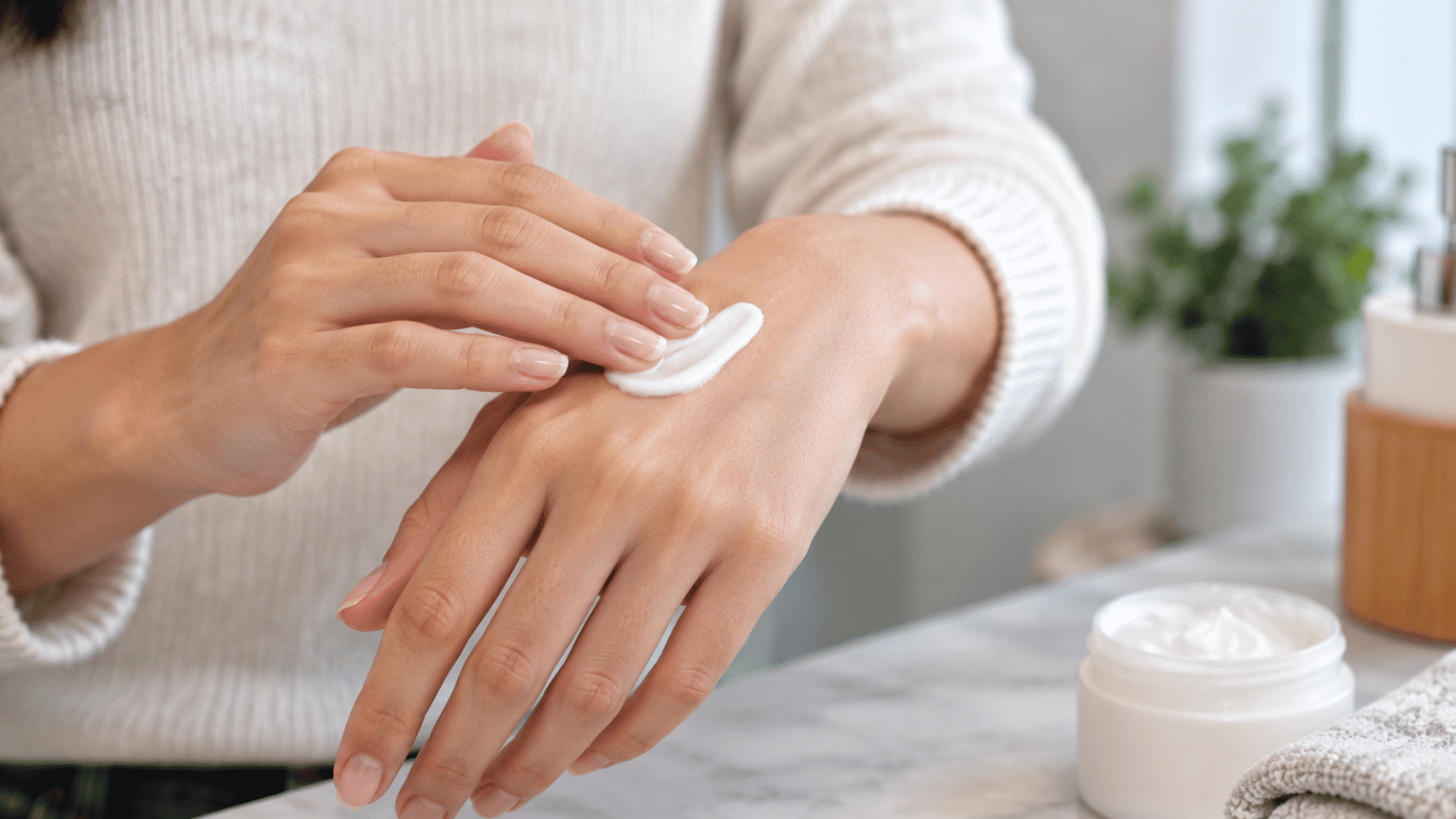 person applying ceramide moisturizer to the back of the hand with cream jar nearby