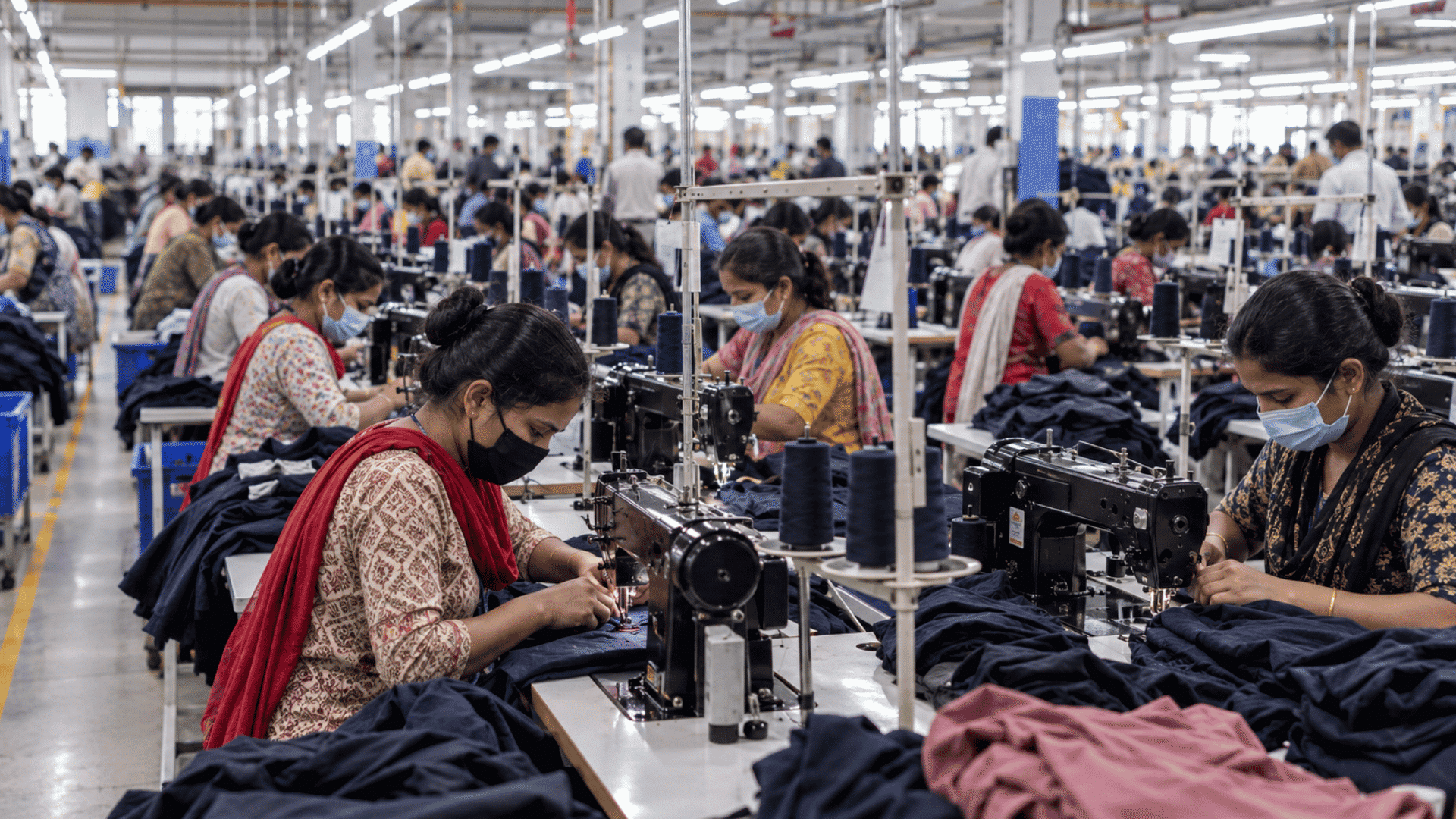 garment workers producing clothing in a large textile factory with rows of workstations and fabric materials