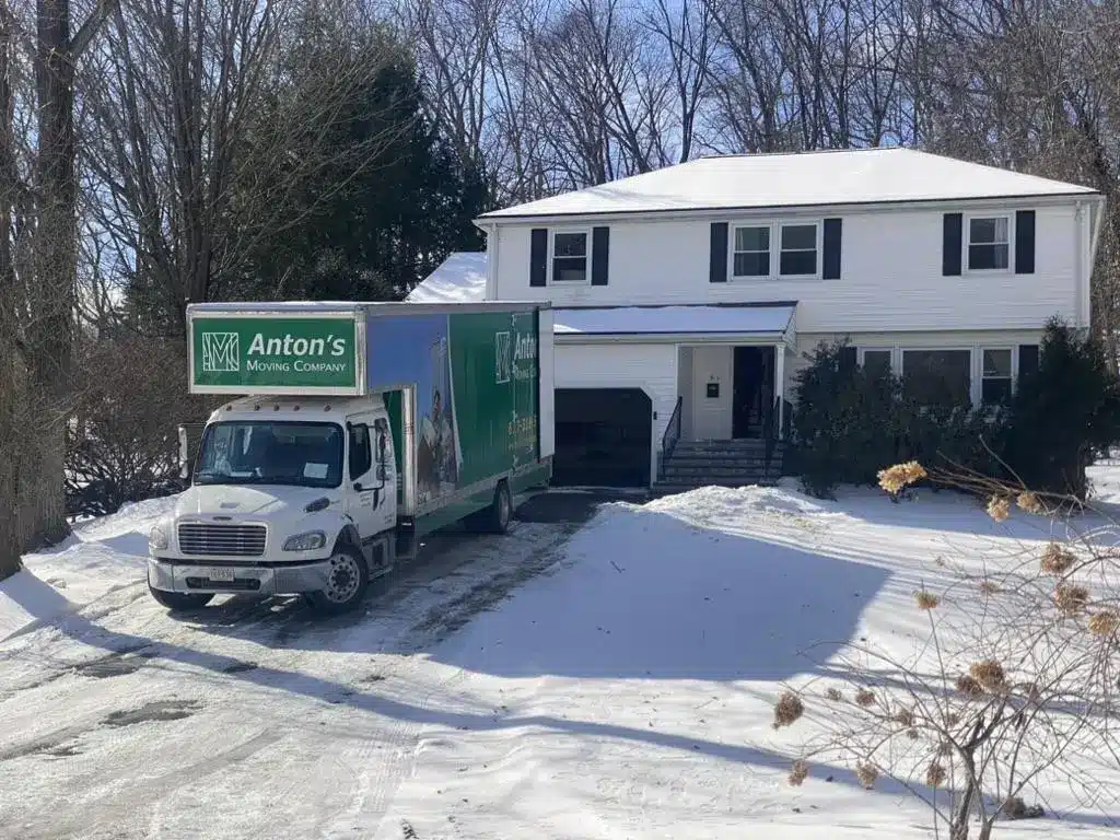 Moving truck parked in snowy driveway of suburban two-story house