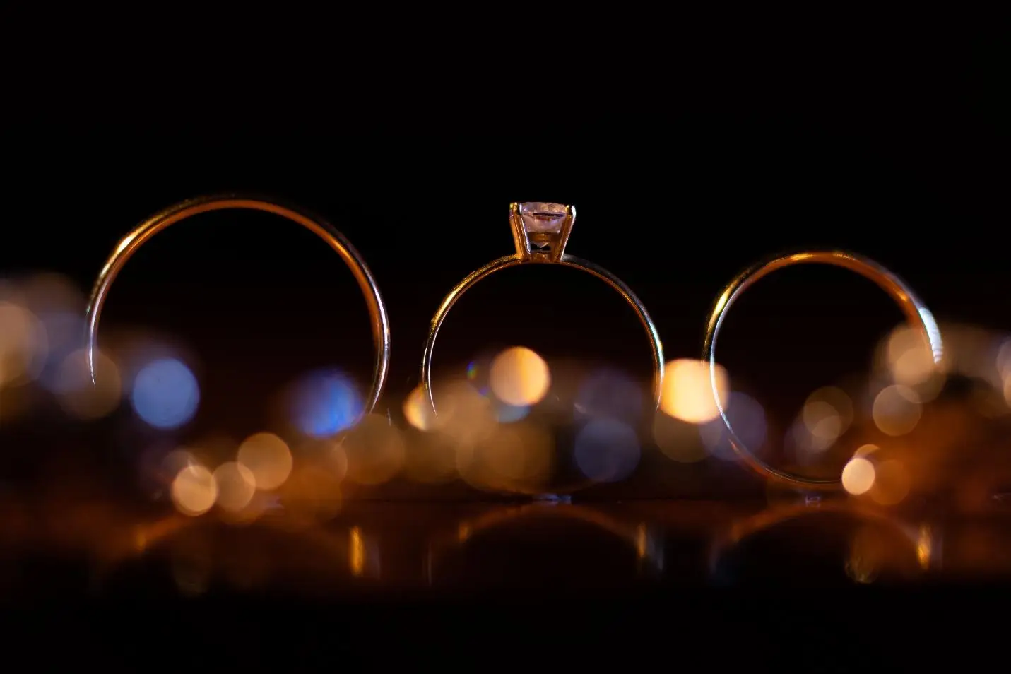 Three rings with a diamond solitaire in dark setting and warm bokeh lights