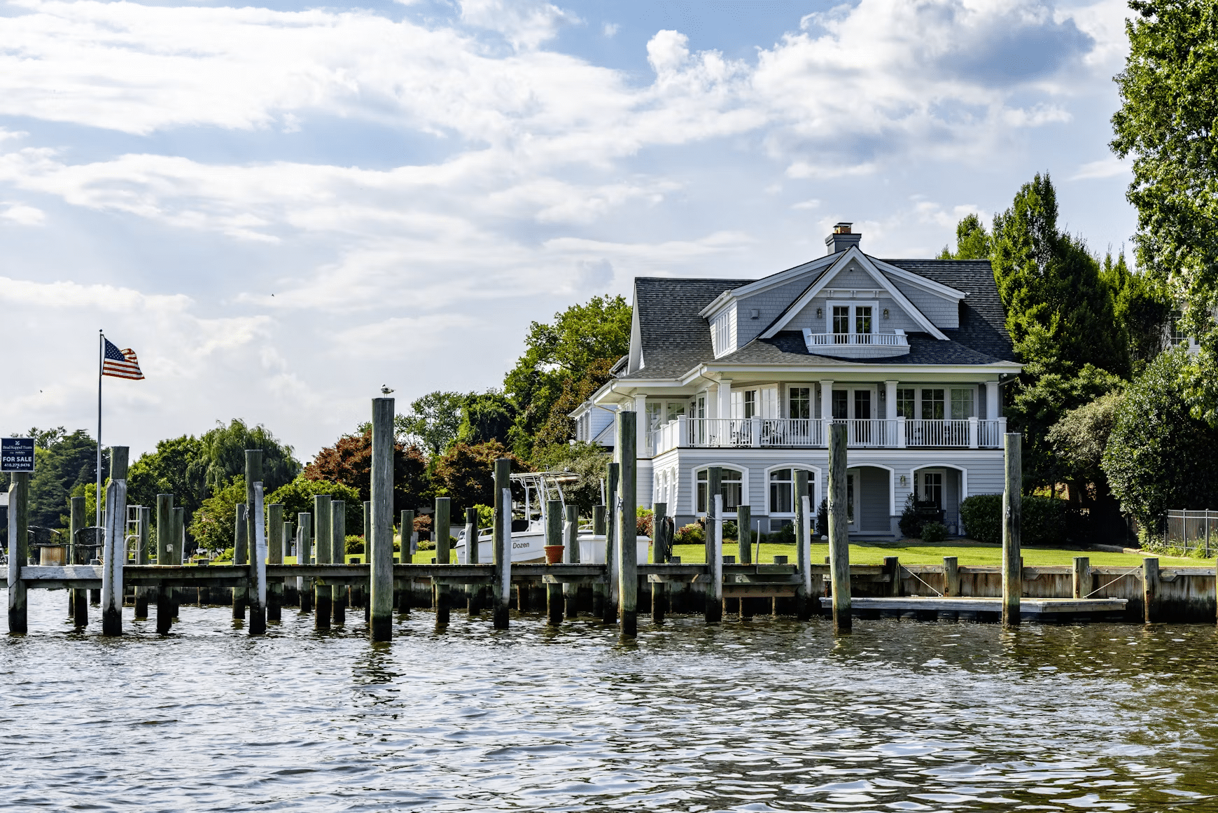 Large white house with balconies near waterfront dock under partly cloudy sky