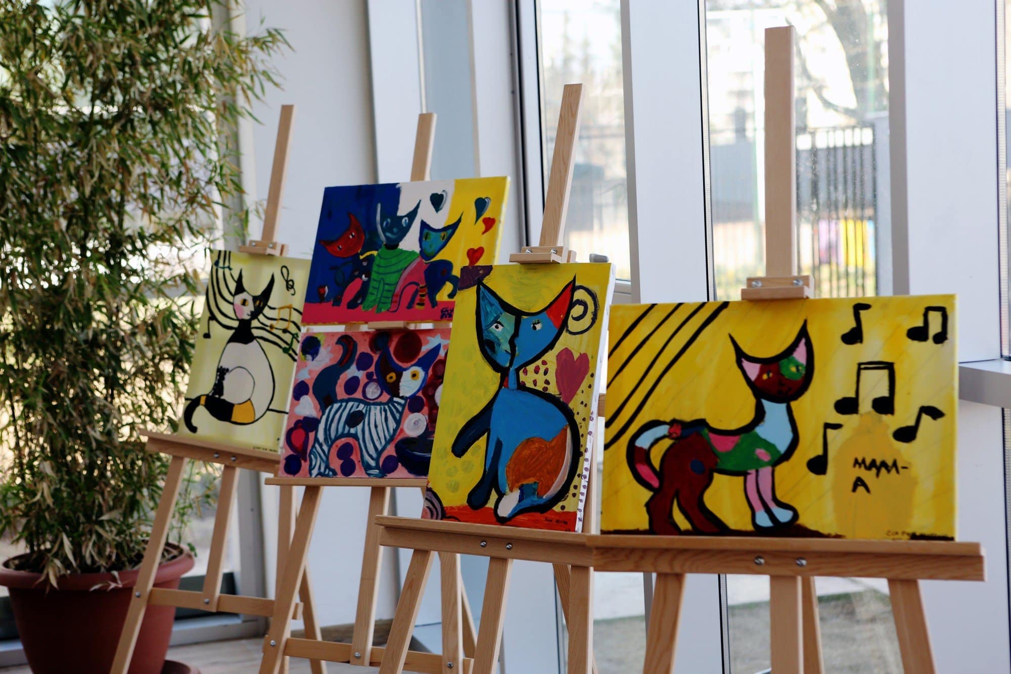 Colorful cat-themed paintings on wooden easels in bright indoor gallery setting