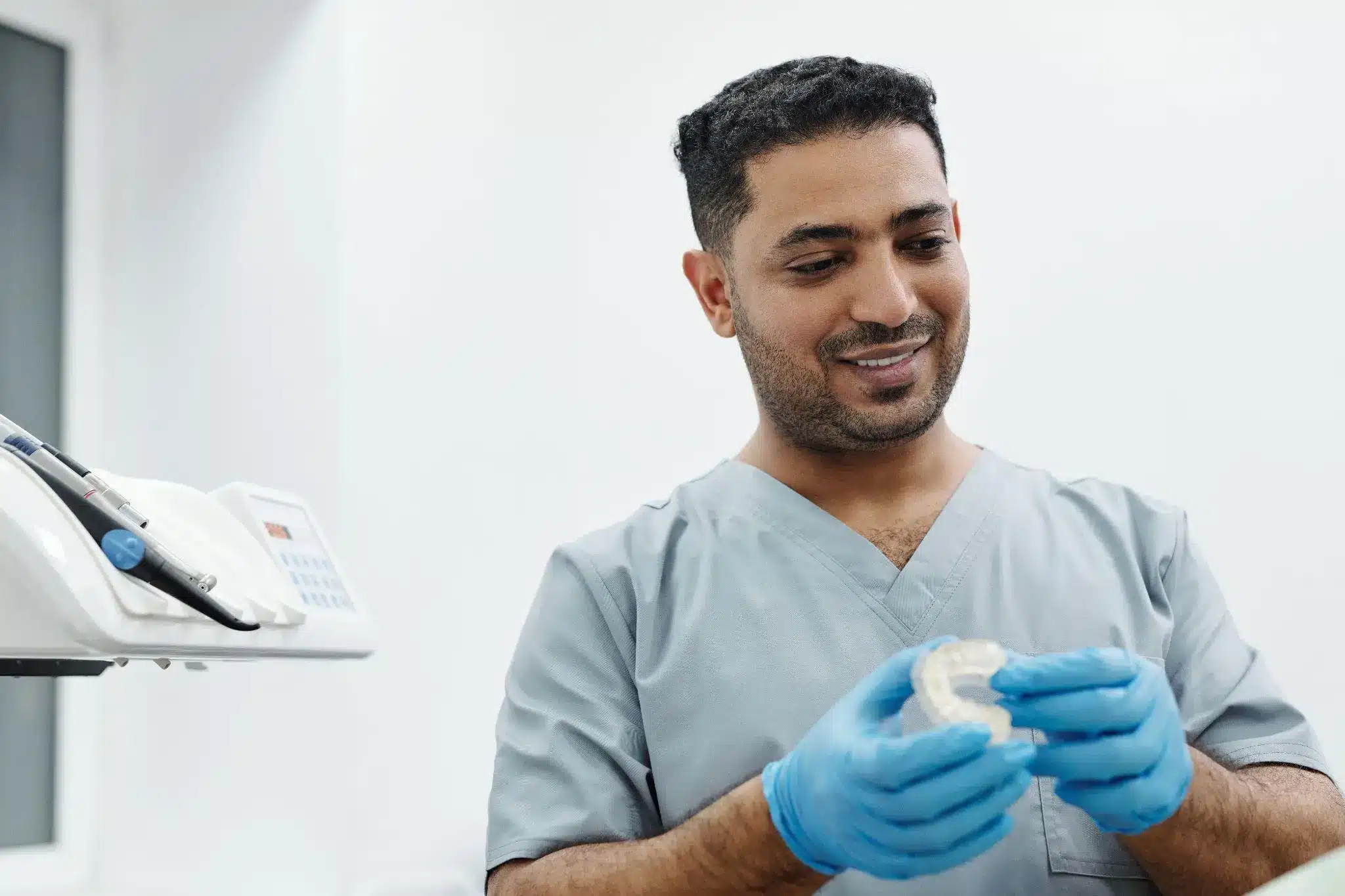 Dental professional examining clear aligner in modern clinical setting with dental equipment nearby