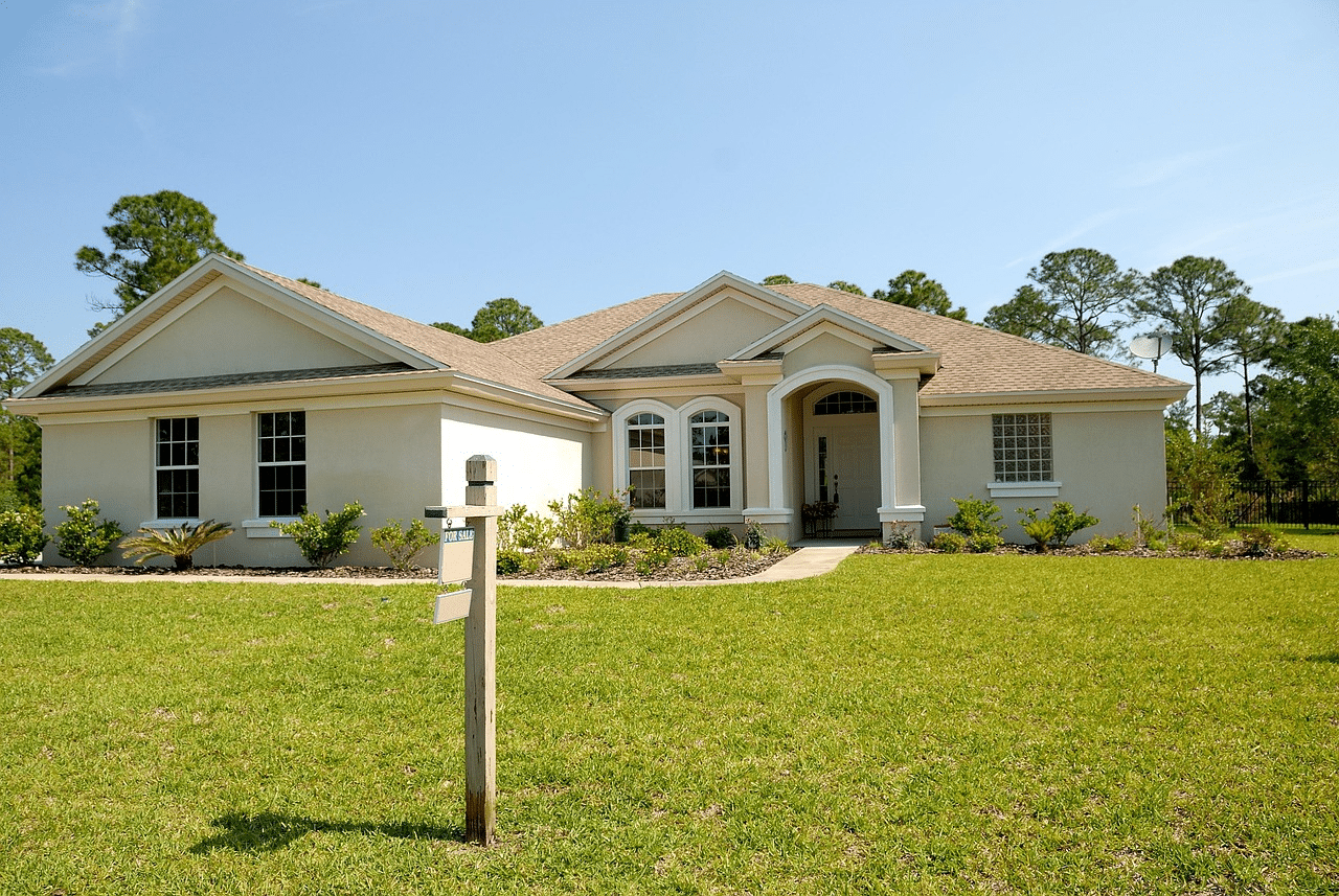 Single-story house with a for sale sign on green lawn under clear blue sky